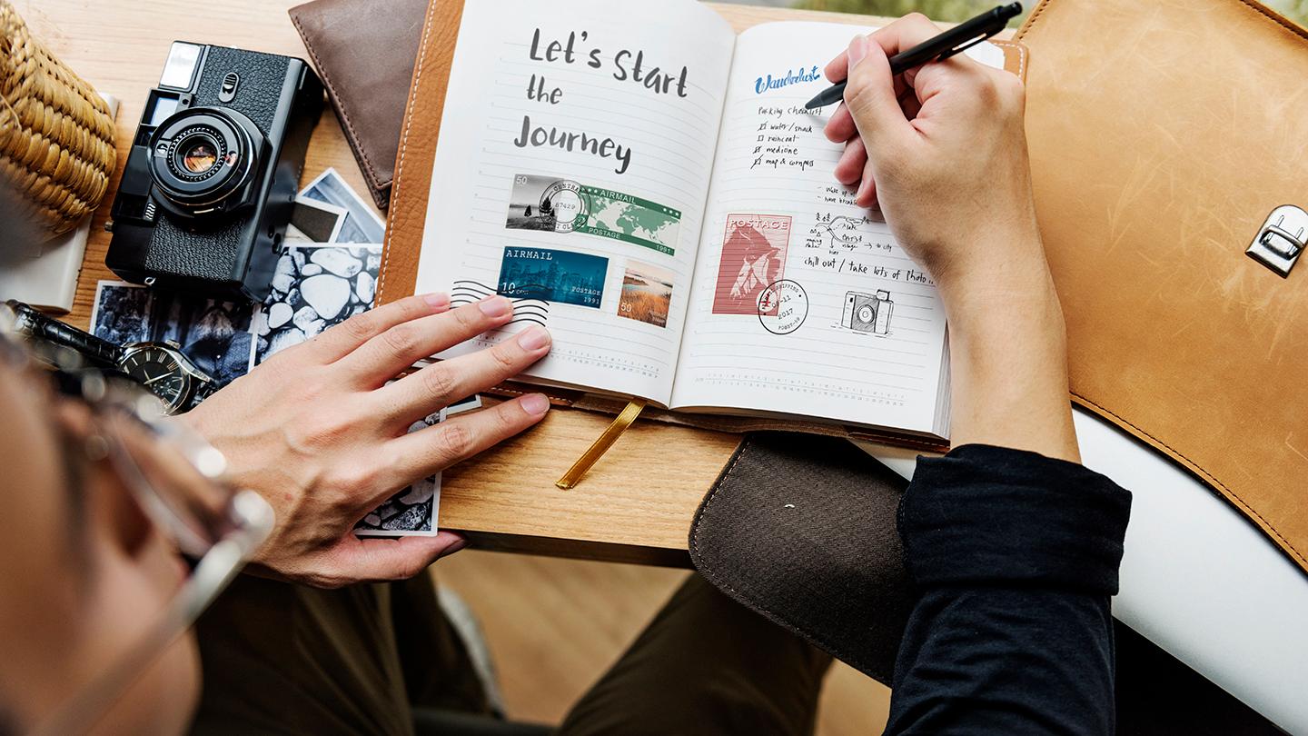 prise de vue d'en haut d'un homme à lunettes entrain d'écrire dans un carnet de notes sur son bureau avec un vieil appareil photo argentique posé à côté de lui